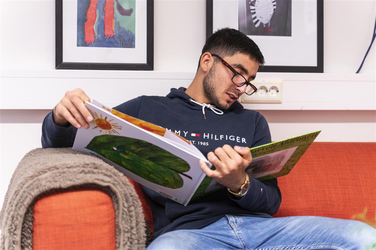 Bilde av elev som sitter i en sofa og leser en bok. - Klikk for stort bilde